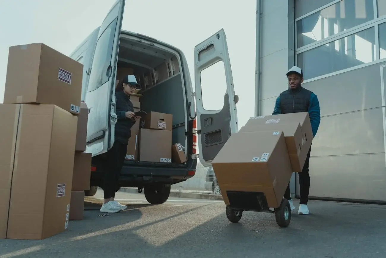 a man pushing a cart with 3 boxes on it and a woman checking conditions on each boxes