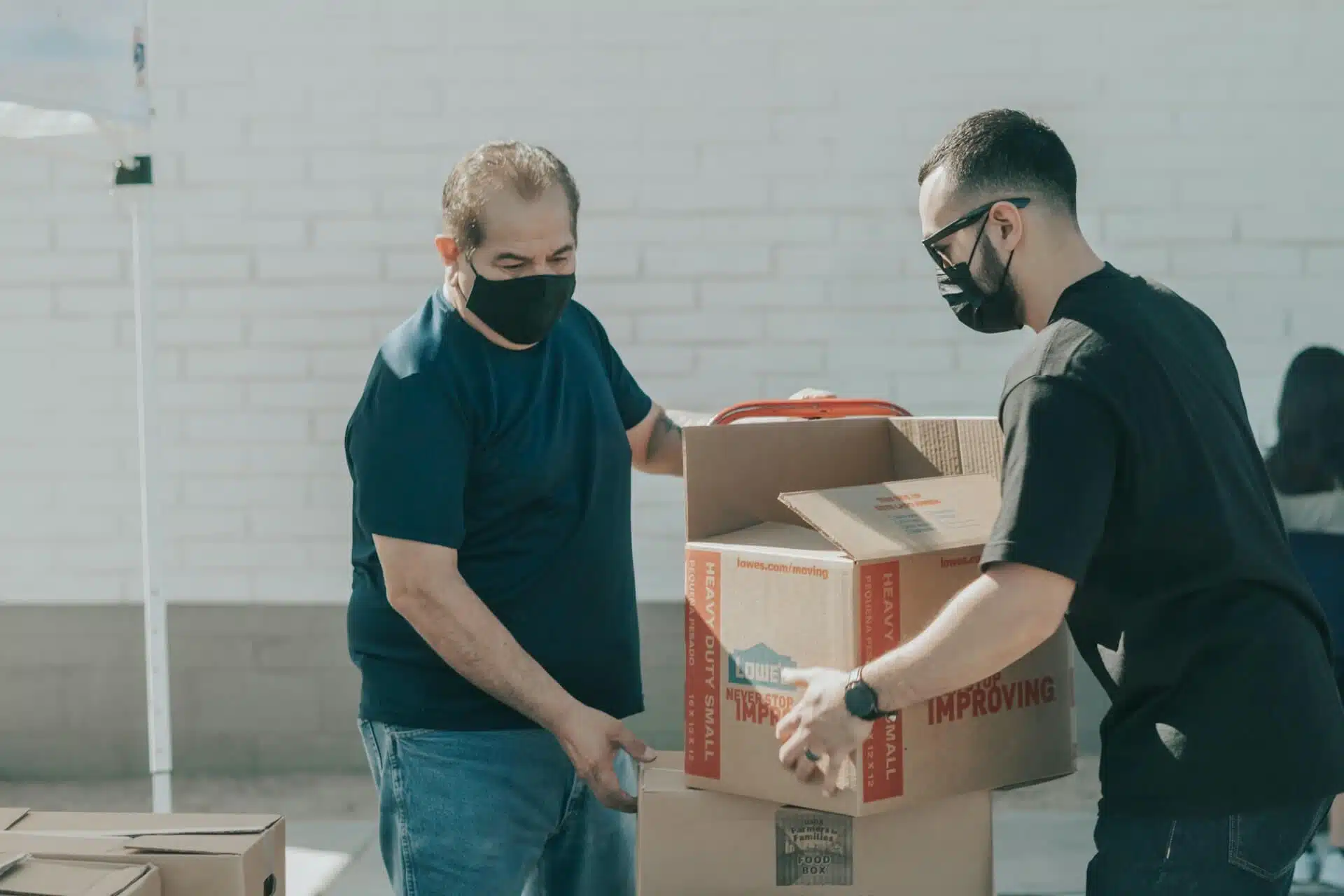 two men wearing a black t-shirt carrying and transferring boxes