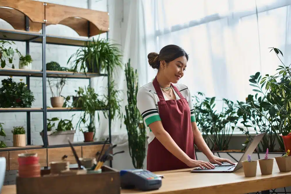 a beautiful asian women working on her laptop and wearing a maroon apron